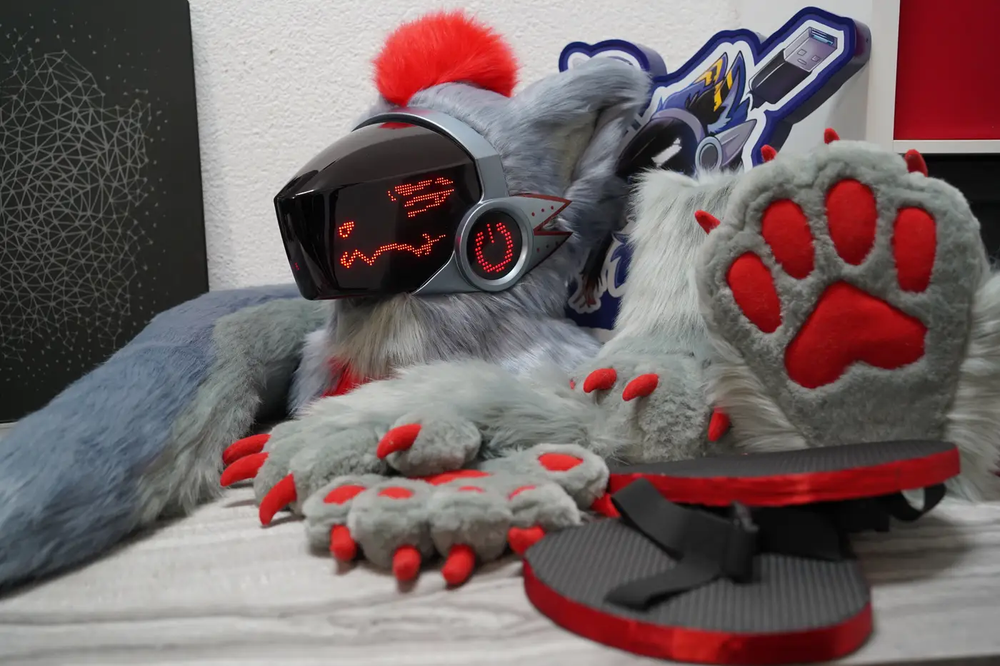 Gray Protogen partial with a red mohawk, a red LED face, a dragon shaped tail, puffy hand paws with red claws and feet paws on black and red outdoor sole sandals