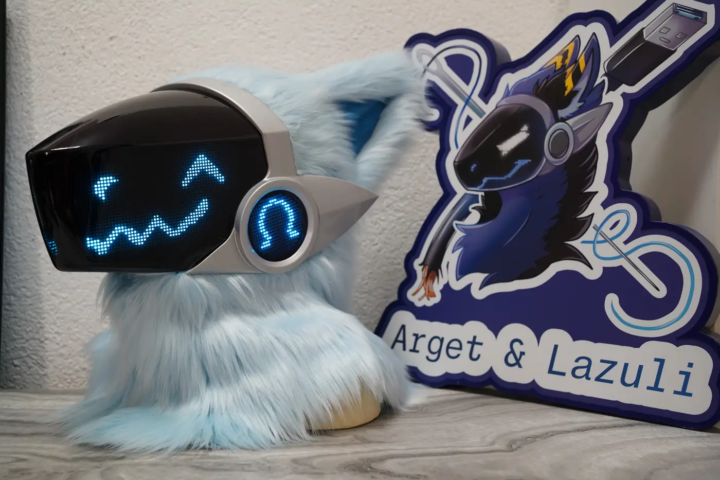 Light blue and silver Protogen head with a blue chevron eye and a long wavy pixel mouth on the LED visor