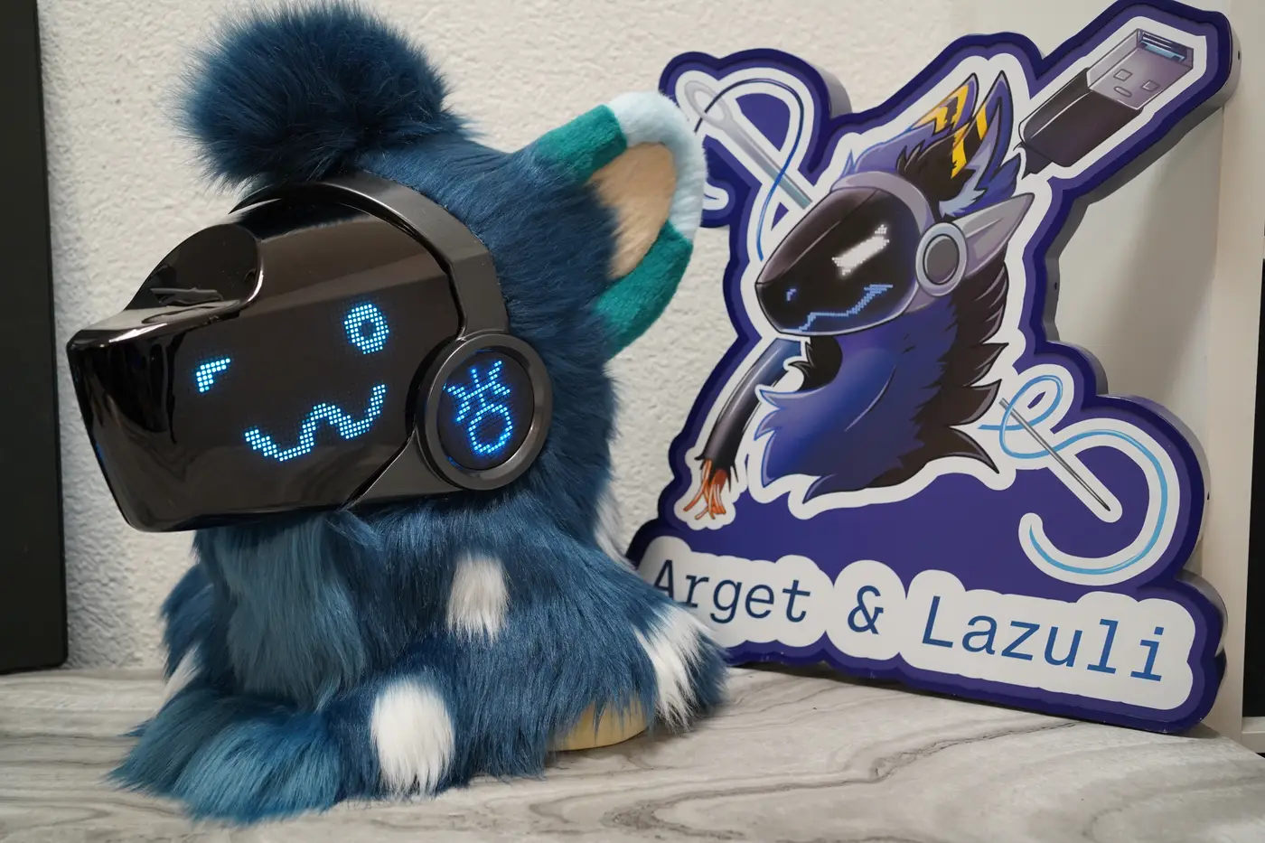 Dark teal Protogen head with a round blue pixel eye and a rounded pixel smile on the LED visor