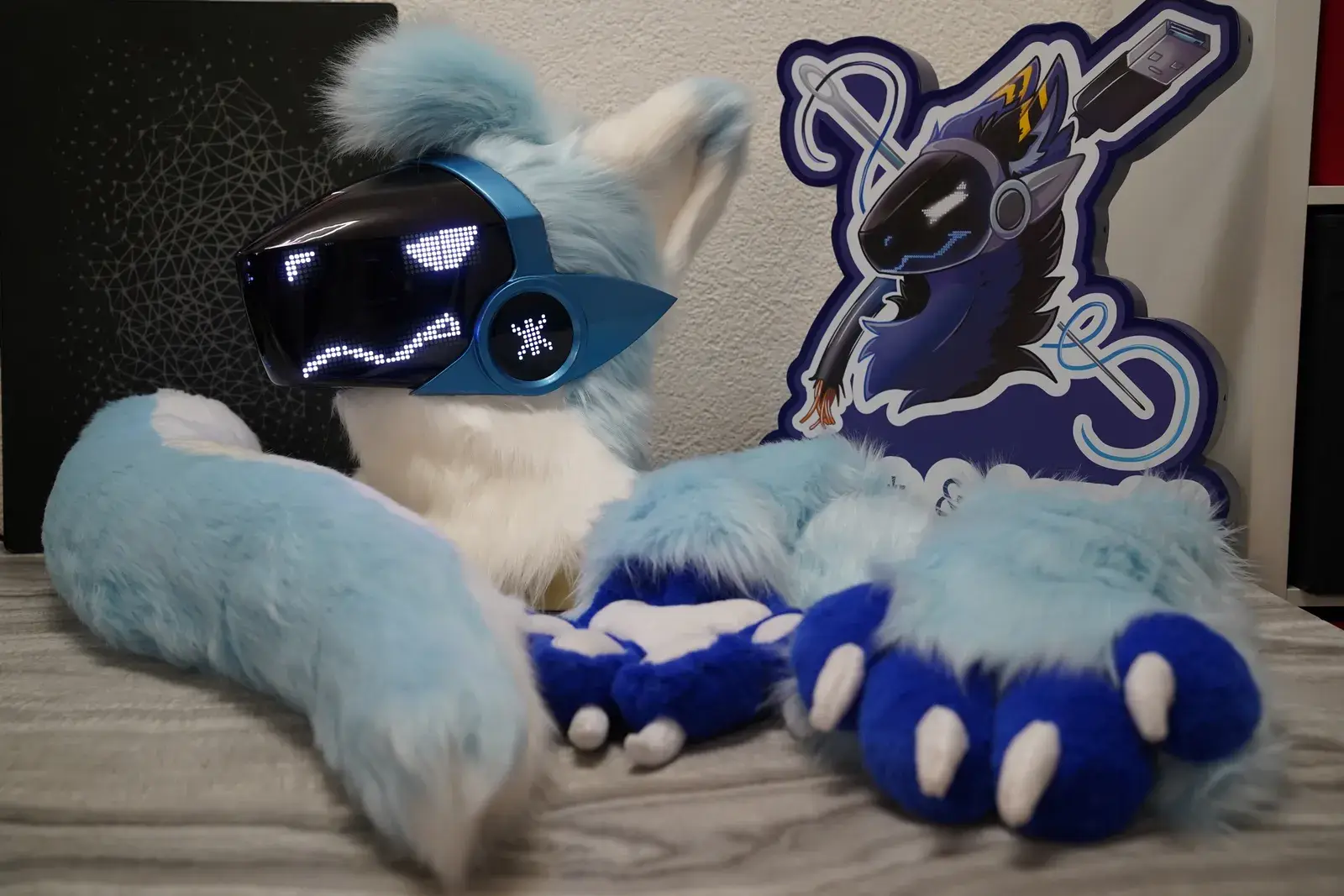 Light blue and white Protogen head with a blue metallic visor showing white pixel eyes, blue hand paws and the Arget and Lazuli logo