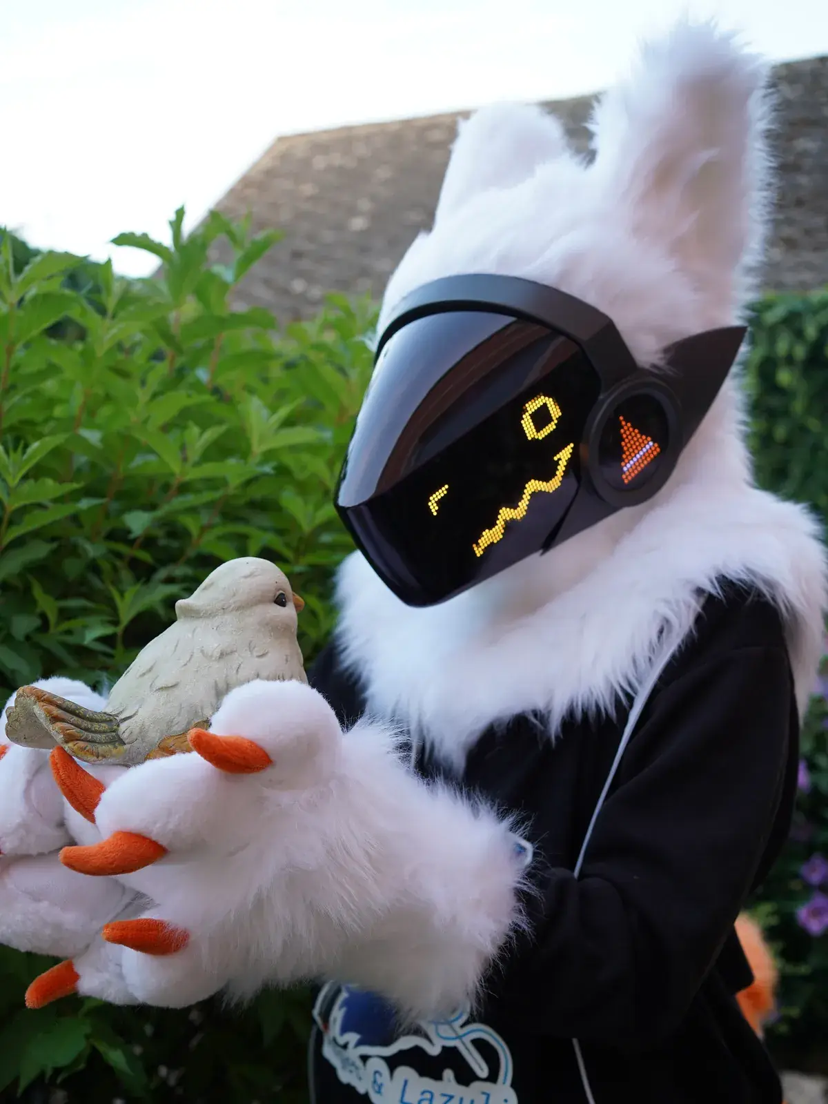 White Protogen mini partial holding a small bird figurine in the garden, orange face on the LED visor