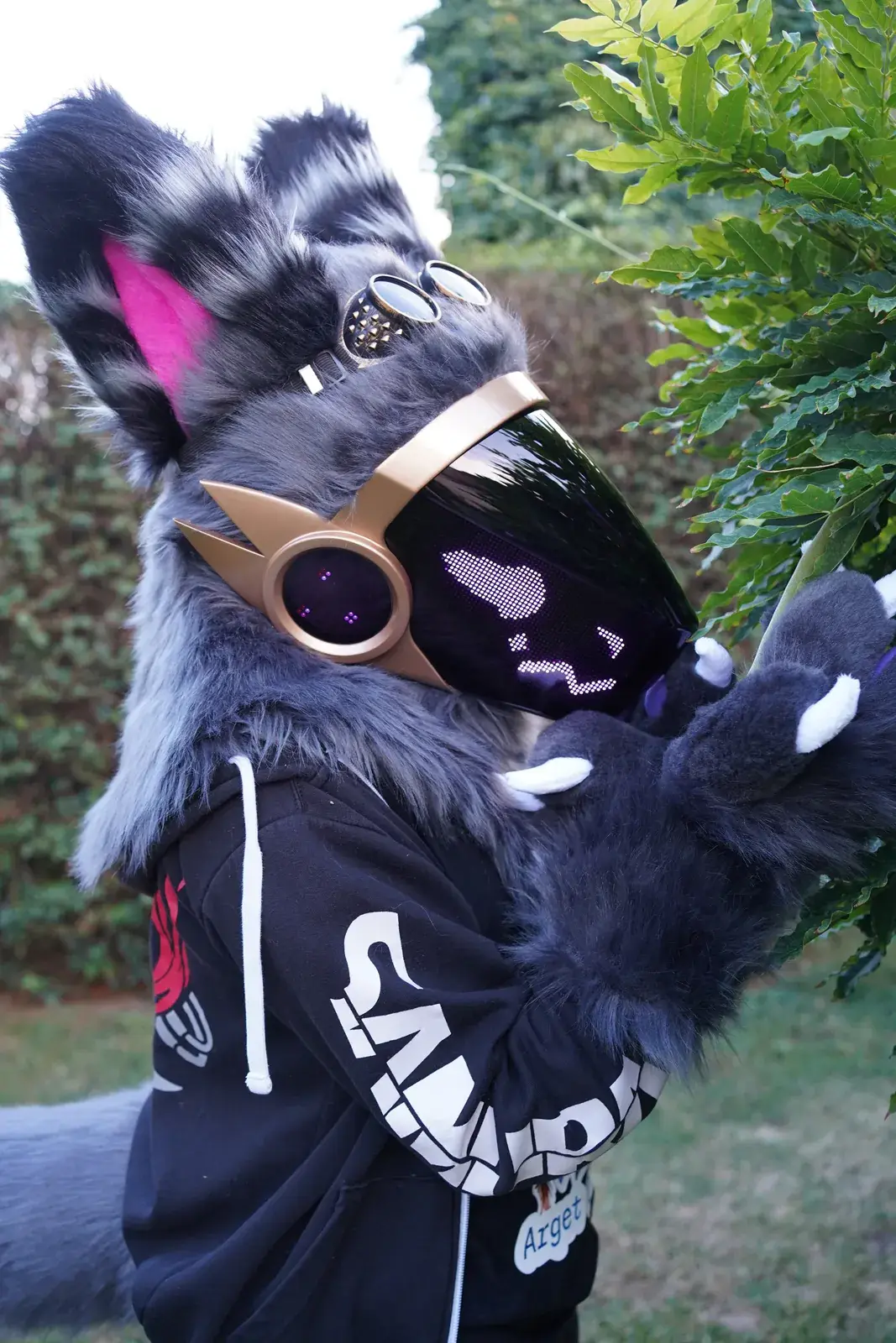 Grey Protogen full partial with goggles on its head reaching into a green garden, purple eyes on the LED visor