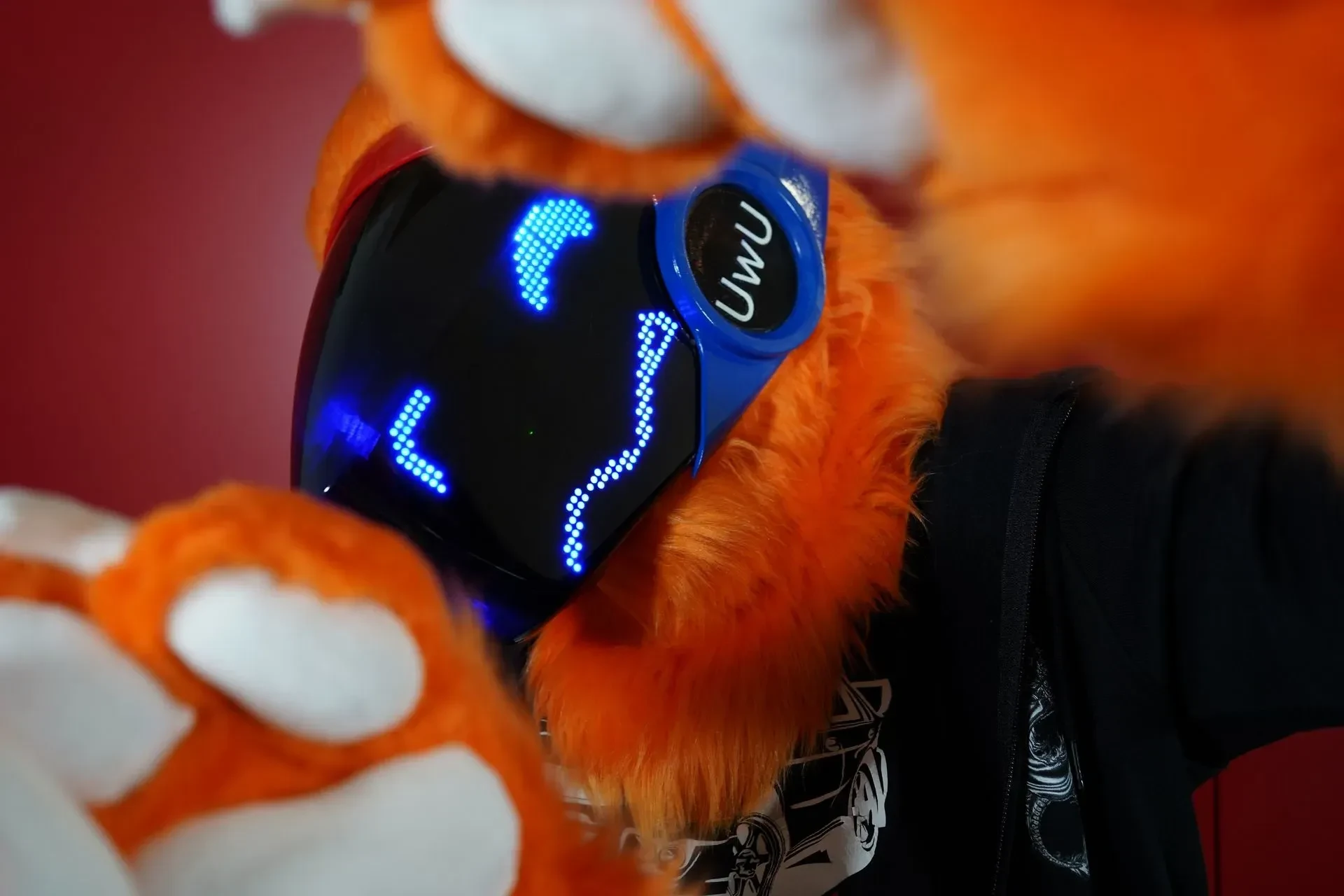 Orange and white Protogen fursuit with a blue LED face and an UwU cheek disc, by Arget & Lazuli